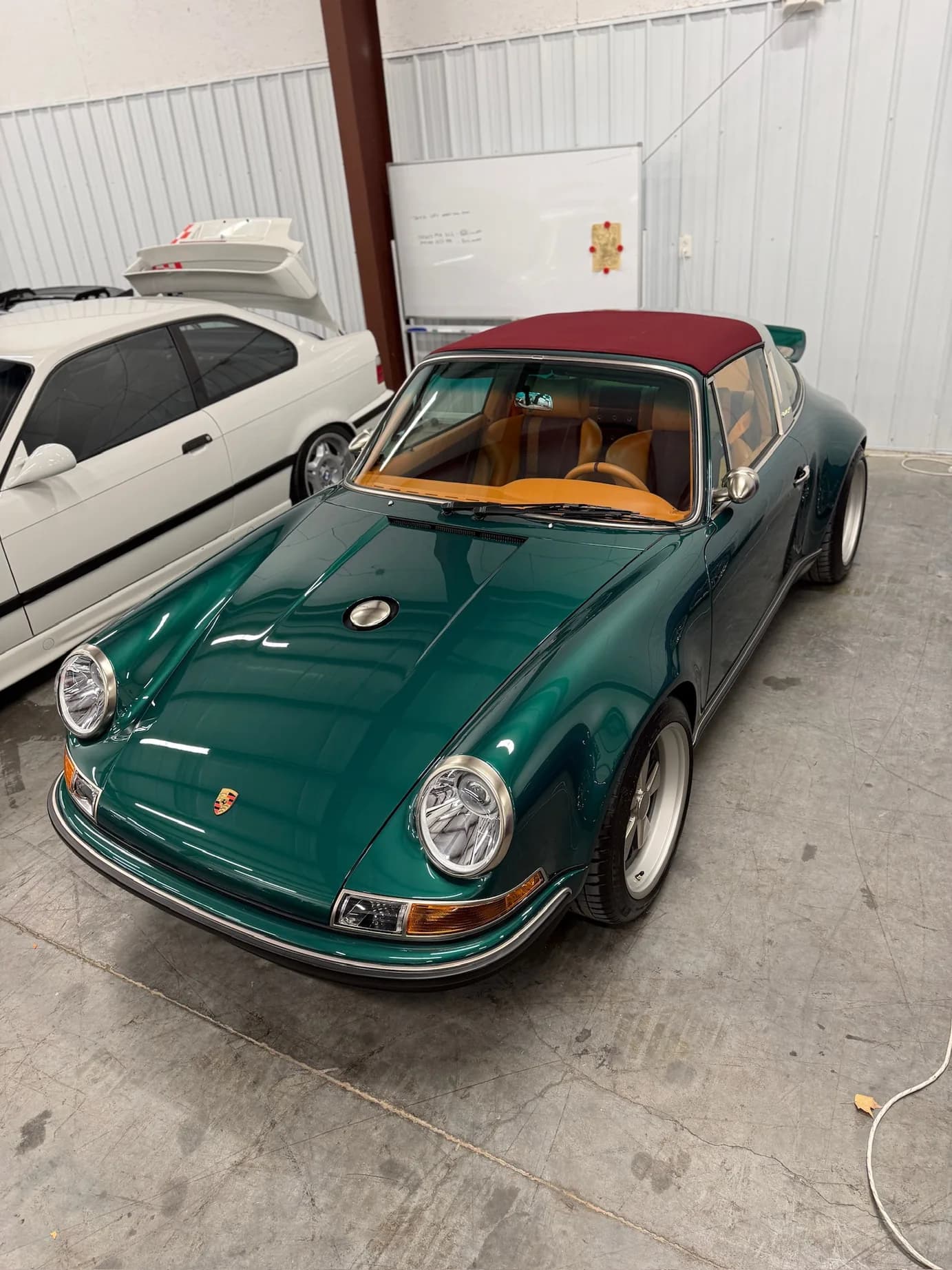 A green Singer-reimagined Porsche 911, targa top up, parked in the shop