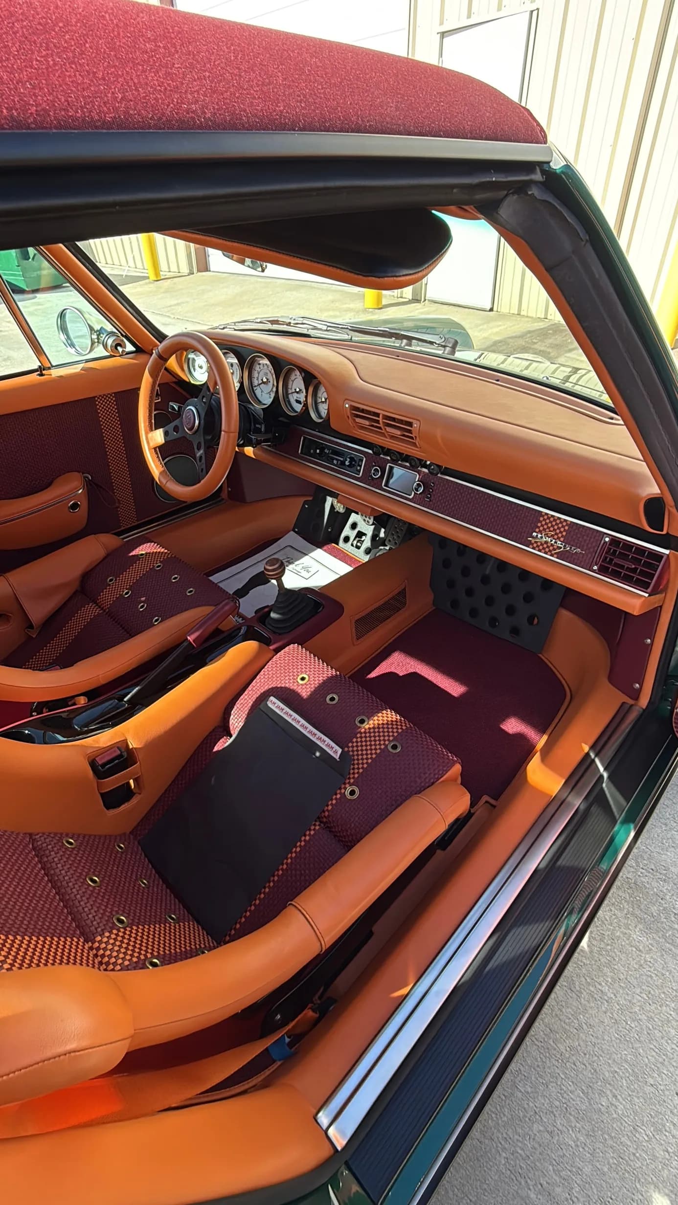 The full cabin, orange leather and burgundy houndstooth, steering wheel and gated shifter visible
